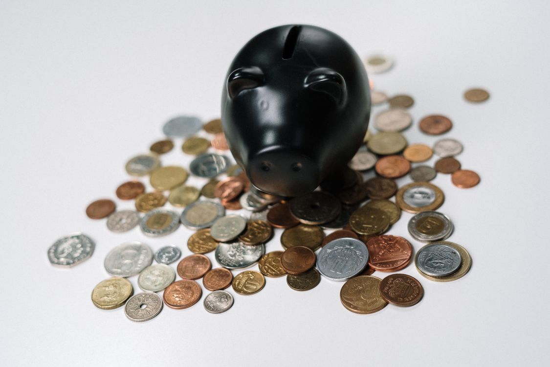 Black piggy bank surrounded by scattered coins on a white background